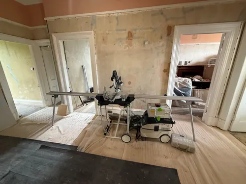 Hallway with bare stripped plaster, hardboard floor protection and a mitre saw and dust extractor set up