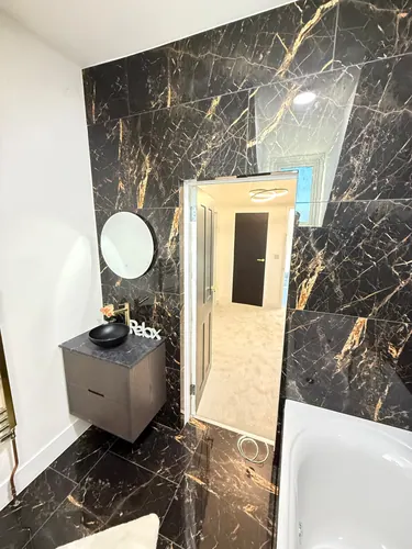 Wall-hung vanity unit with black countertop basin, round mirror and tiled walls