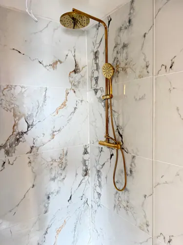 Brass rainfall shower and riser fitted against marble-effect tiling