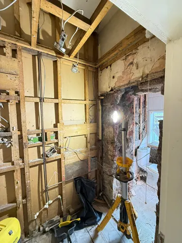 Open studwork with new cables dropped in and a work light in the corner