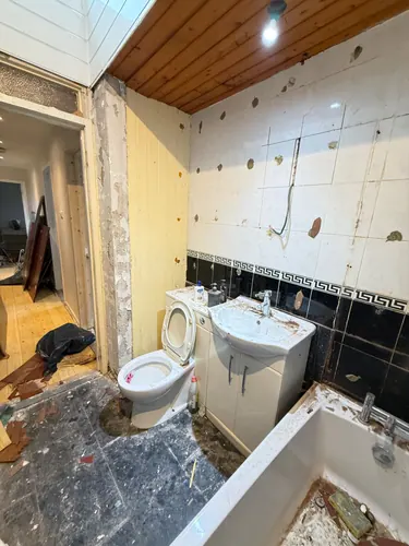 Toilet and vanity basin awaiting removal beside stripped tiled walls