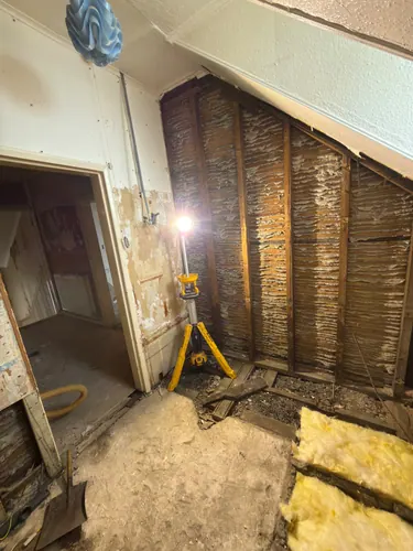 Lath walls exposed under the coombed ceiling with a work light set up