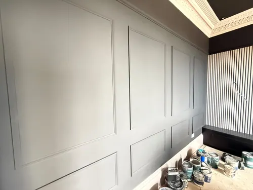 Painted grey panelling alongside a slatted feature wall and built-in bench, paint tins on the floor
