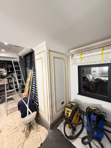 Joiner fixing panel mouldings to a boxed column with dust extractors and ladders in place