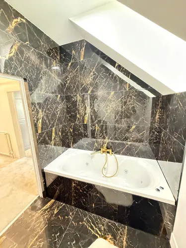 Finished bath with brass taps under the tiled coombed ceiling and downlight