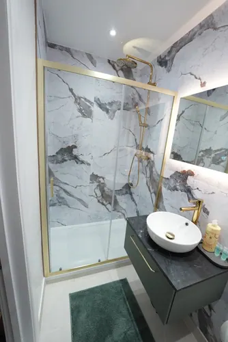 Sliding door shower enclosure with brass rainfall shower and marble-effect panels