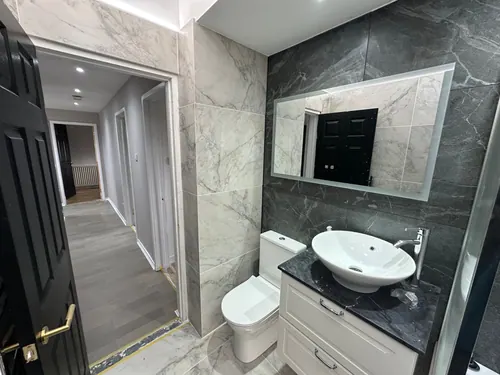 Toilet, vanity and illuminated mirror on the dark tiled wall looking out to the hall