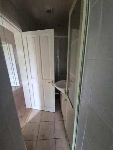 Hall doorway into the old shower room with dated floor tiles and a basin unit