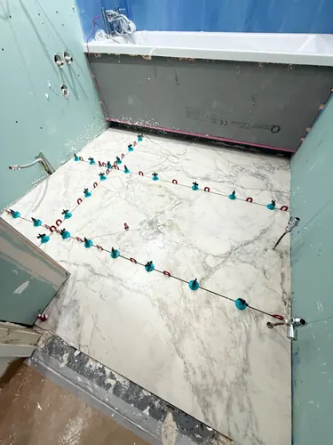 Marble-effect floor tiles laid with levelling clips against boarded walls and new bath