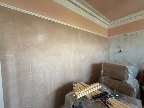 Bare plaster wall below original cornice with panel mouldings and tools on a covered surface