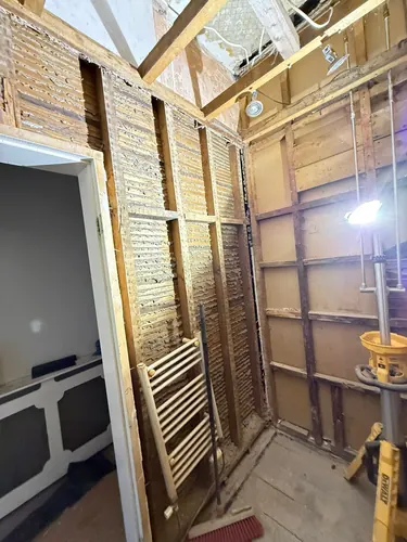 Shower room stripped to studs with old lath visible and towel radiator removed