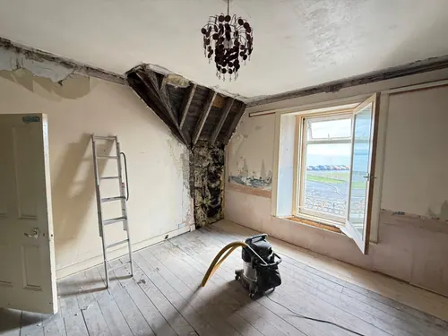 Bedroom before work with damaged plaster, exposed ceiling joists and bare floorboards
