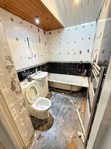 Old bathroom part stripped with tiles being knocked off and bath still in place