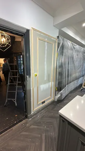 Caulked and filled panel section next to a doorway with plastic sheeting protecting the run of units