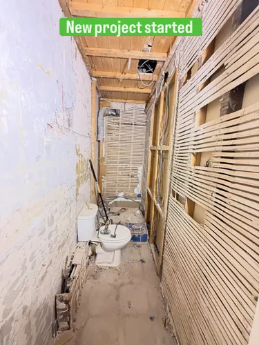 Narrow WC stripped to lath and plaster with old toilet still in place and ceiling joists exposed