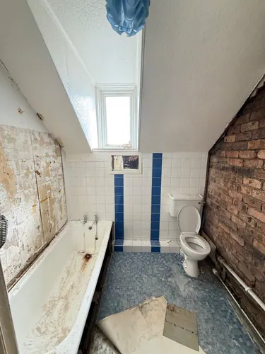 Old attic bathroom with stained bath, blue-striped tiling and exposed brick wall
