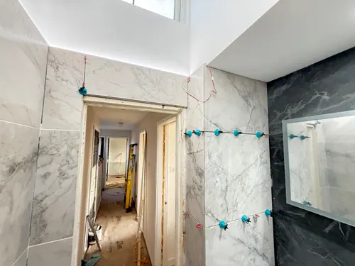 Tiled walls and illuminated mirror with doorway to the hall