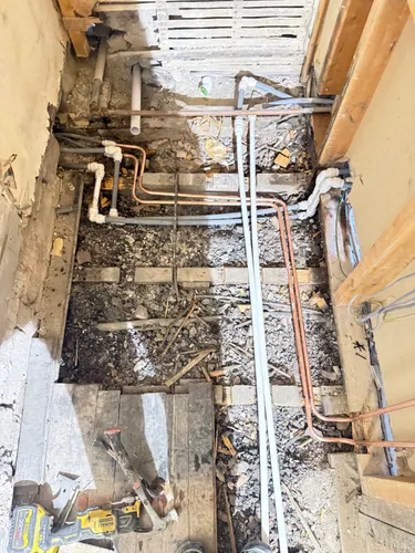 Floorboards lifted showing new copper and plastic pipework and cabling run between the joists