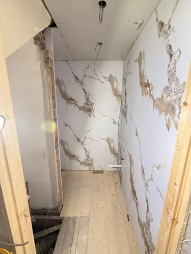 Marble-effect wall panels going up with shower cable and pipe stubs showing