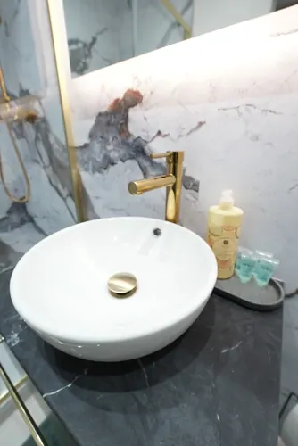 Round countertop basin with tall brass mixer tap on a dark worktop