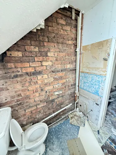 Bare brick wall, surface-run pipework and old toilet before work started