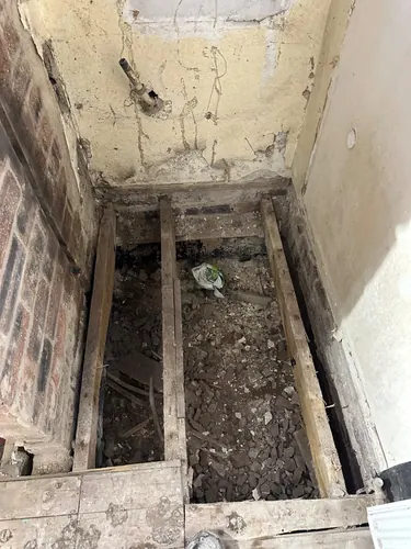 Floorboards lifted showing joists, rubble and old waste pipe
